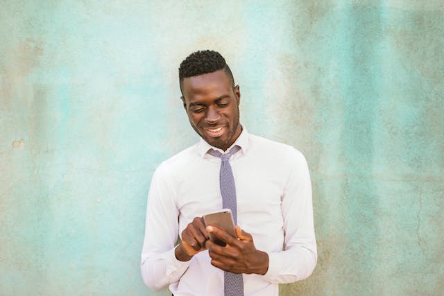 Un homme sourit tout en naviguant sur son téléphone. 