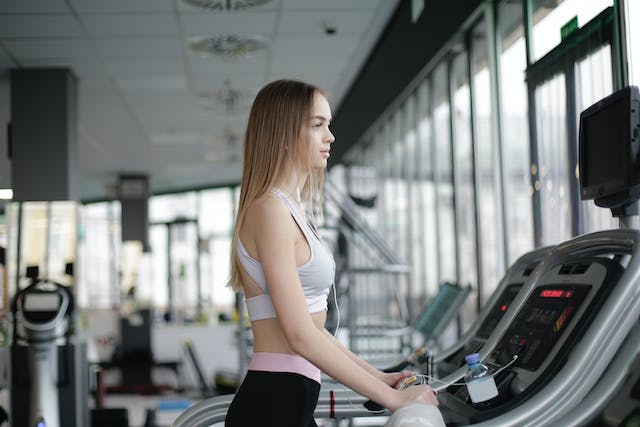 A photo of a woman standing on a treadmill. 