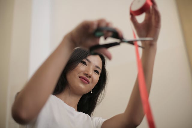 A woman cuts a red ribbon with a pair of scissors. 