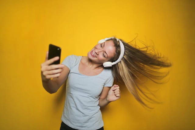 Eine Frau hört und tanzt mit ihrem Handy und Kopfhörern zu Musik. 