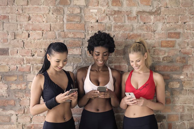 Drie vrouwen in sportkleding bladeren online op hun telefoon. 