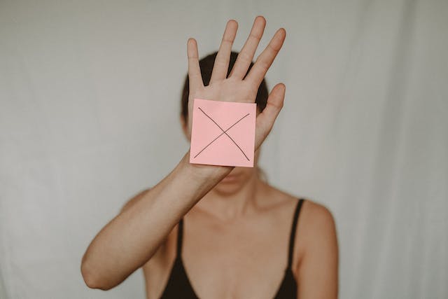 A photo of a woman showing a post-it on her hand with the letter X printed on it. 