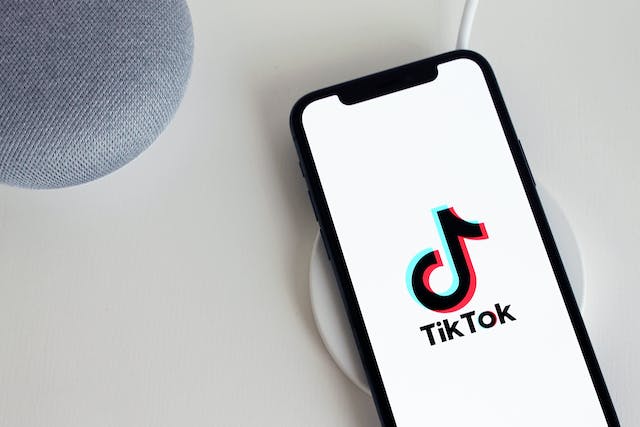 Auf dem Bildschirm eines Telefons erscheinen der schwarze TikTok-Name und das Logo auf weißem Hintergrund. 