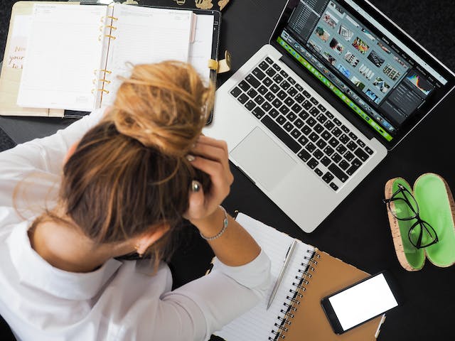 Une femme est assise devant son ordinateur portable, la tête entre les mains. 