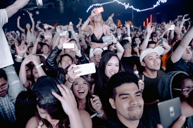 An excited crowd takes photos of performers on a stage.