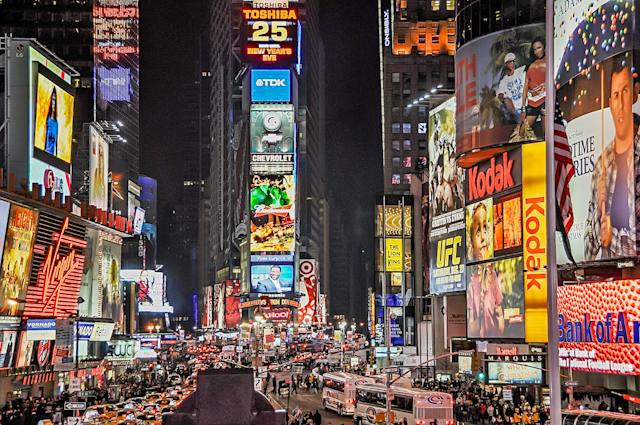 Una foto di una strada trafficata di notte con cartelloni pubblicitari digitali sugli edifici. 
