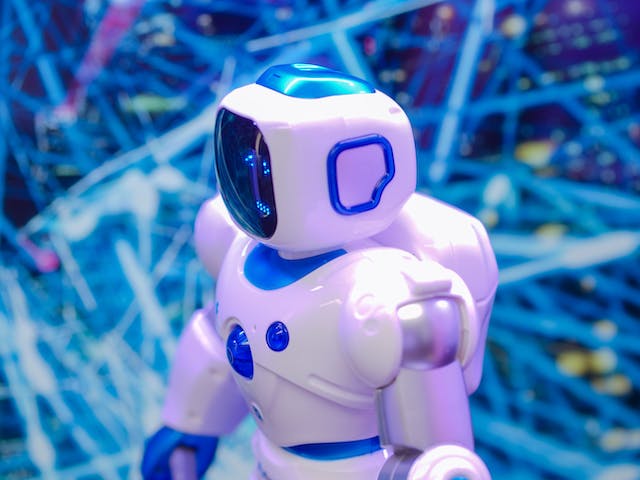 A photo of a small blue and white bot standing in front of intersecting blue lines. 