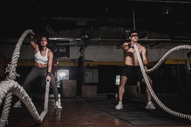 A man and woman exercise with battle ropes at the gym. 