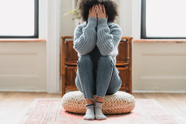 A woman sits on the floor while she covers her face with her hands.