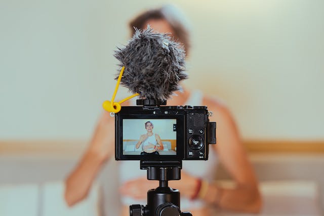 A woman stands in front of a camera for a live stream. 