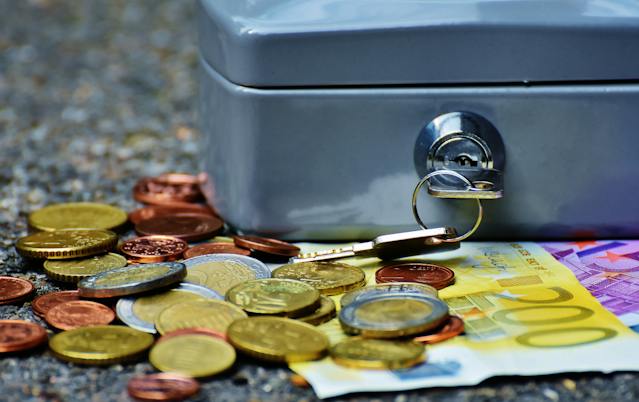 An image of a cash box with a key in the lock and some coins and bills around it. 