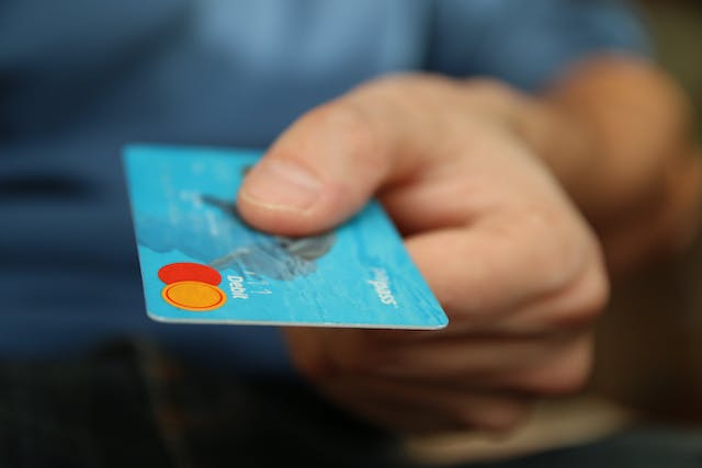 A person holds out their debit card to make a payment. 