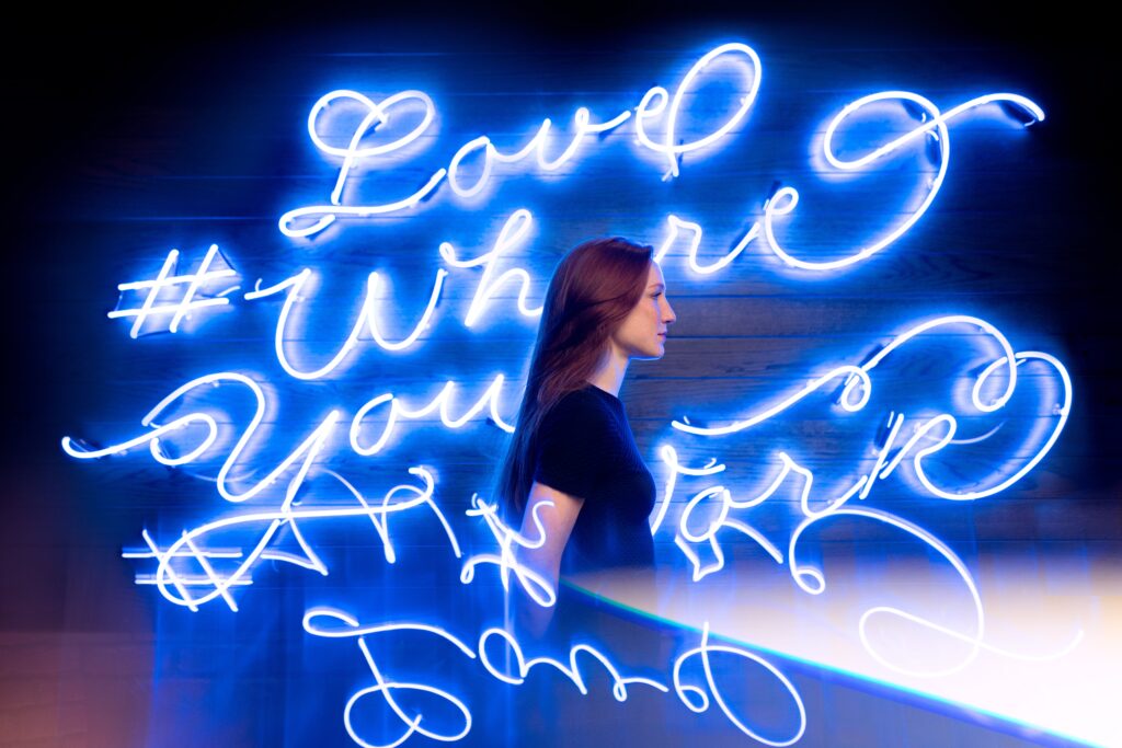 Blue neon signs featuring various hashtags surround a woman. 
