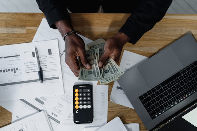 Des billets de banque sont éparpillés sur une table tandis qu'une personne utilise une calculatrice. 