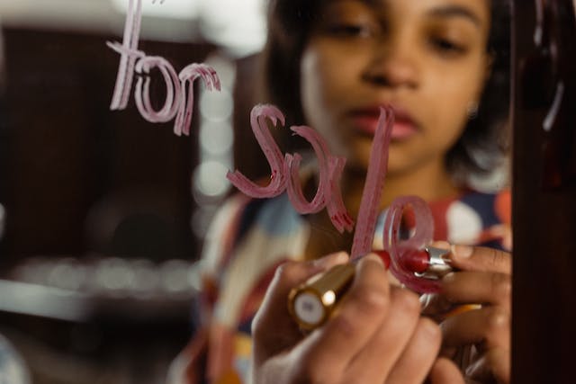  A woman writes “For Sale” on a mirror using lipstick. 