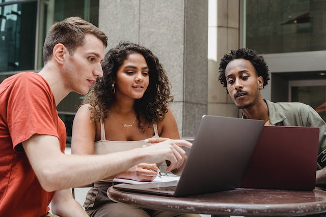 Three young adults browse online content on their laptops. 