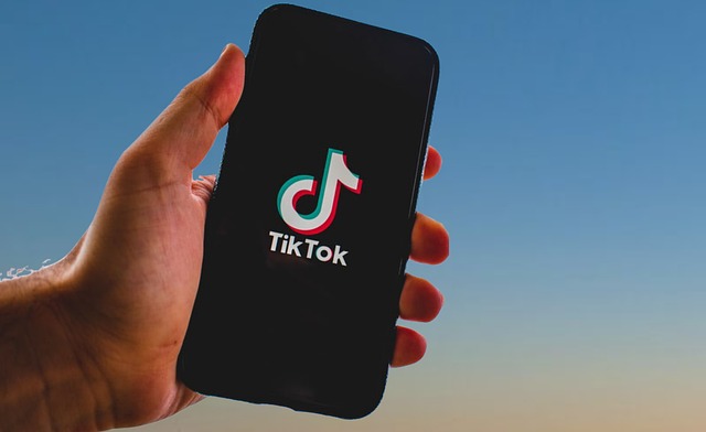 TikTokのロゴが入った黒い携帯電話を持つ人の手のアップの写真。