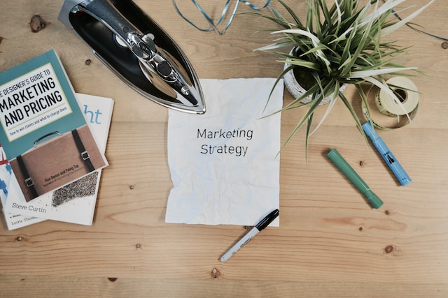 Photo d'un papier avec les mots "MARKETING STRATEGY" et d'un livre de marketing sur une table en bois.