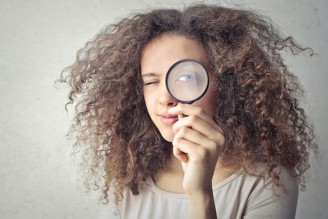 A woman holds a magnifying glass in front of one eye. 