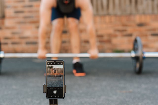 A man films himself while lifting weights. 