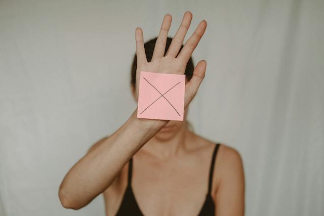 A woman holds up her hand with a Post-it note showing the letter X. 