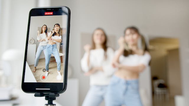 Two women dance in front of a camera for a TikTok video. 