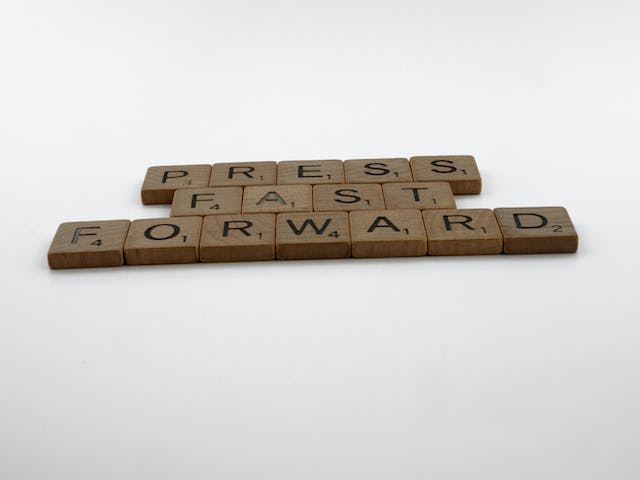 Wooden letter tiles spell the word “PRESS FAST FORWARD.”