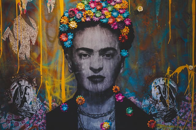 A photo of a wall graffiti featuring Frida Kahlo in black and white and with colorful flowers. 