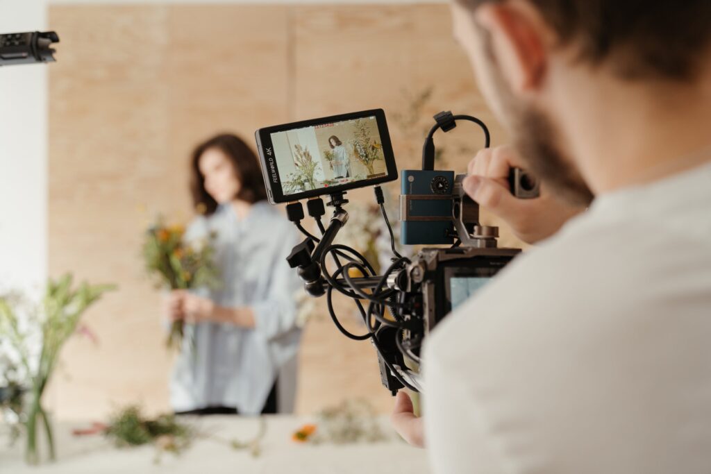 A man films a woman arranging flowers. 