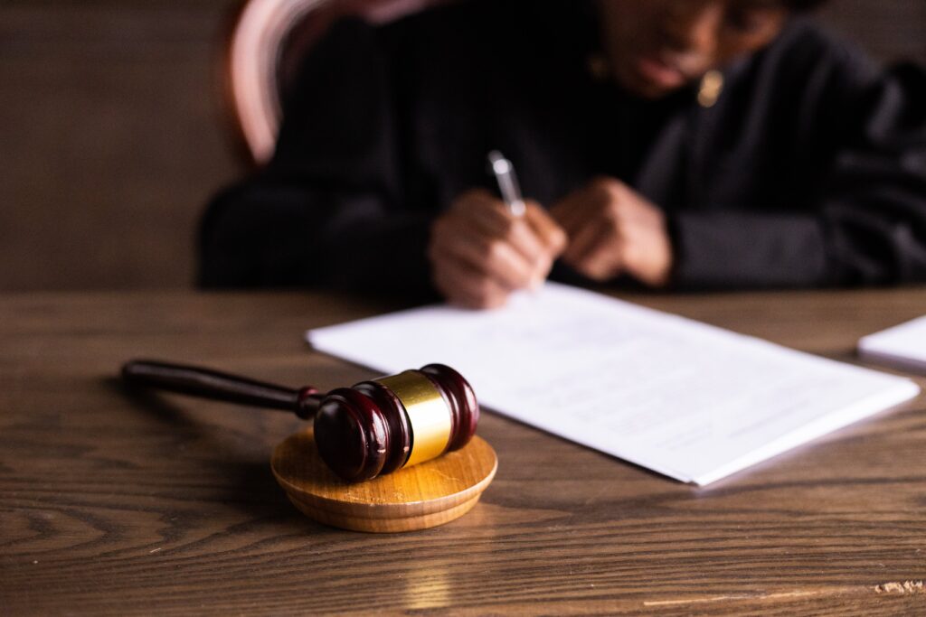 小槌のクローズアップ画像と、書類に署名する裁判官の後ろ姿。 