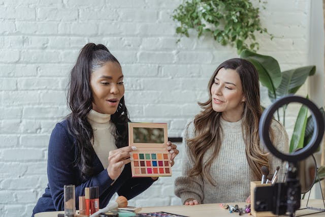 Imagen de dos mujeres grabando un vídeo con productos de maquillaje. 