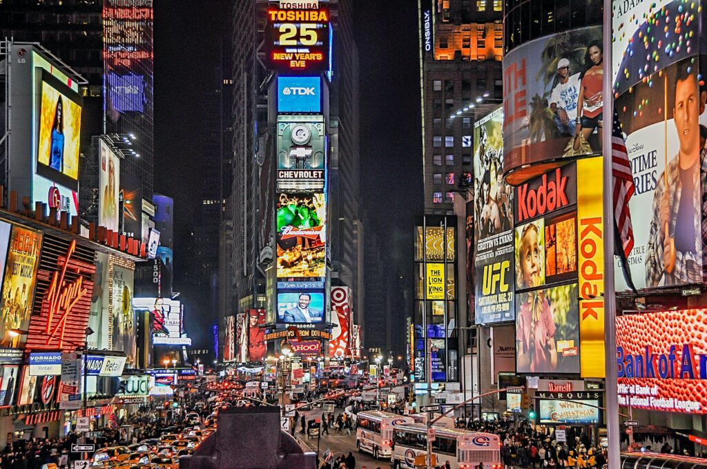 An image of a city at night alight with giant digital ads on buildings. 