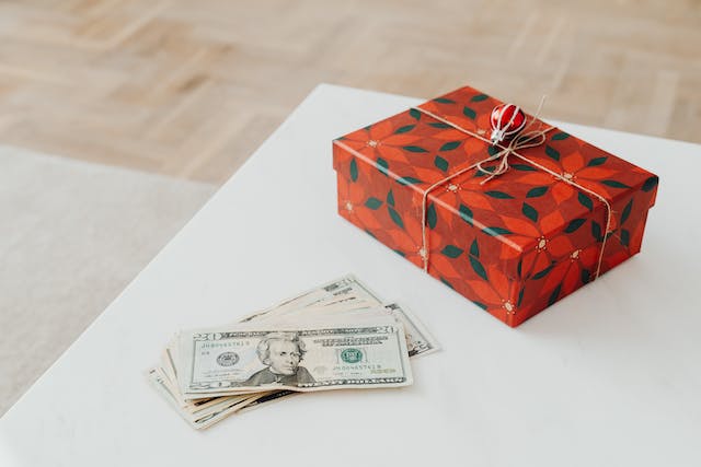Una scatola regalo rossa e alcune banconote da un dollaro su un tavolo. 