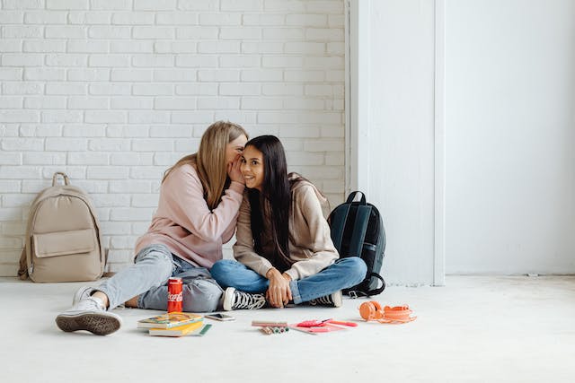 Uma imagem de uma jovem sussurrando no ouvido de sua amiga. 