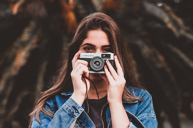 O femeie ține un aparat de fotografiat în fața feței sale. 