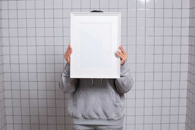 A person hides behind an empty picture frame. 