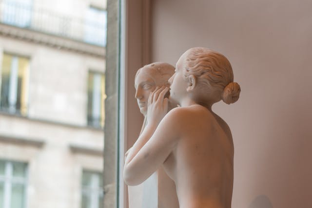 A photo of a statue of two people beside a window. 