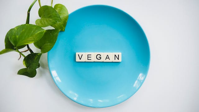 An image of a blue plate with white letter tiles that read, “VEGAN.”