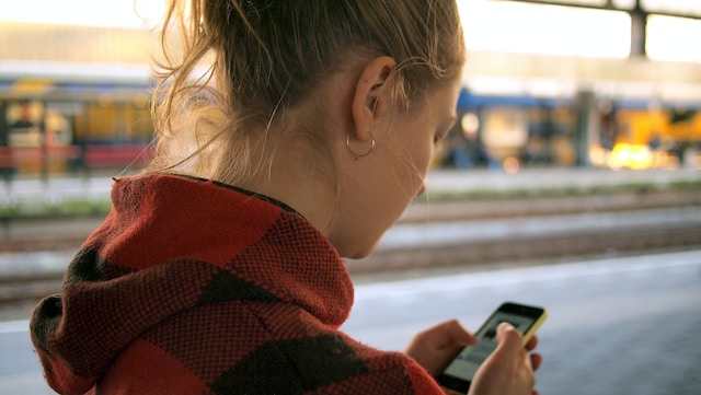 O imagine cu o doamnă care vizualizează conținut pe telefon în timp ce se află pe un drum.