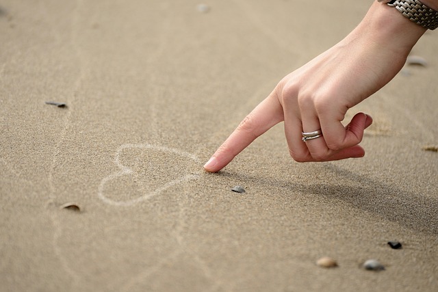 A picture of a hand drawing the heart icon on the sand.
