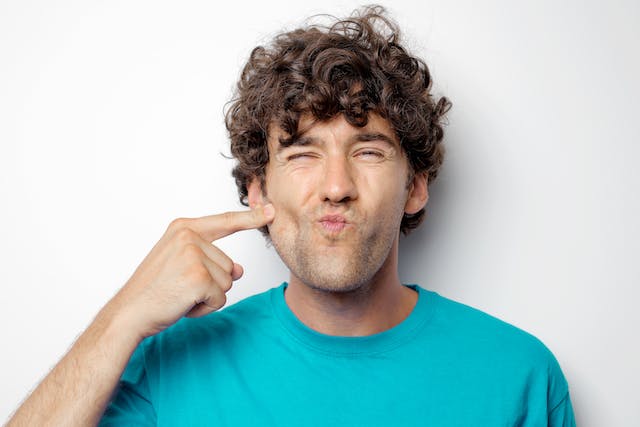 A photo of a man gently poking his cheek with a finger. 
