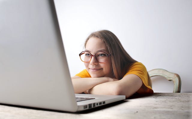 A woman wearing spectacles watches TikTok videos on her laptop. 
