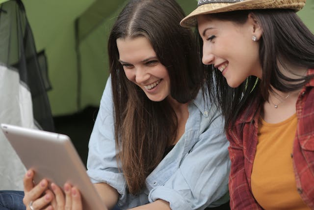 Duas mulheres jovens rindo enquanto olham para um tablet. 