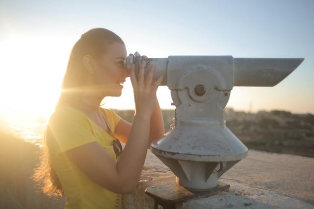 A woman uses a viewing scope on top of a roof. 