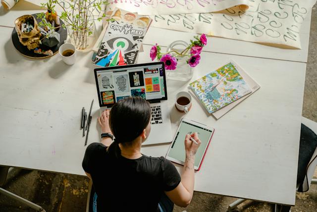 Toma aérea de una mujer que trabaja con su portátil y crea arte digital en una tableta. 