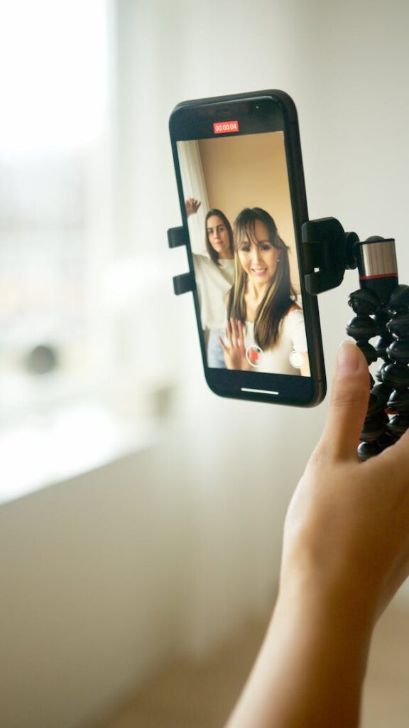 Two women use a phone on a tripod to record a video of themselves in selfie-mode.