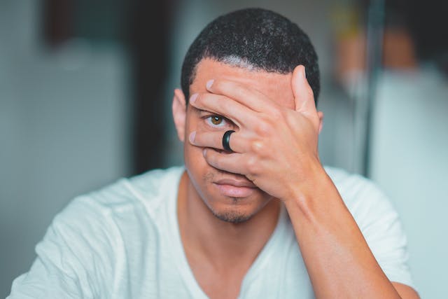 Un homme se couvre le visage d'une main et regarde entre ses doigts. 