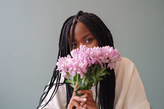 A woman covers the bottom half of her face with a bouquet of pink flowers. 