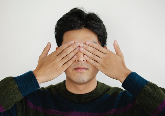 A man is covering his eyes with both hands. 