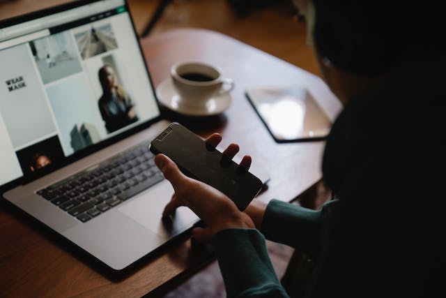 Uma mulher navega em seu laptop enquanto segura um telefone. 